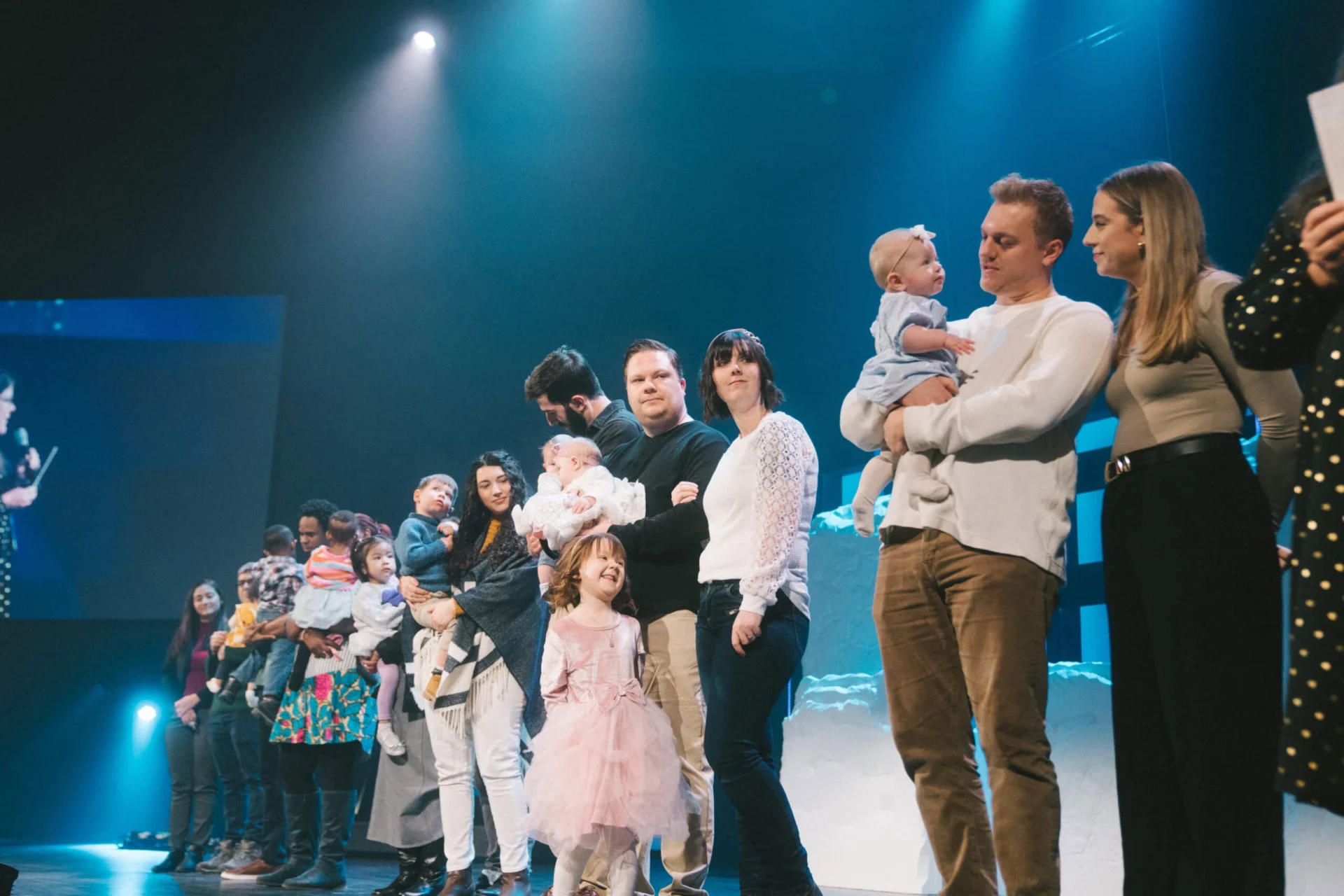Several families with their babies and young children lined up across the stage during a child dedication.