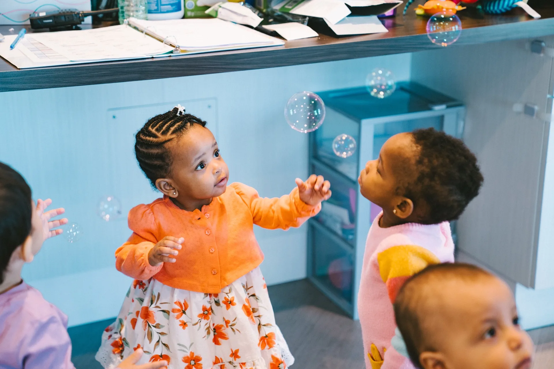 Two toddlers reaching for bubbles in a bright childcare room.