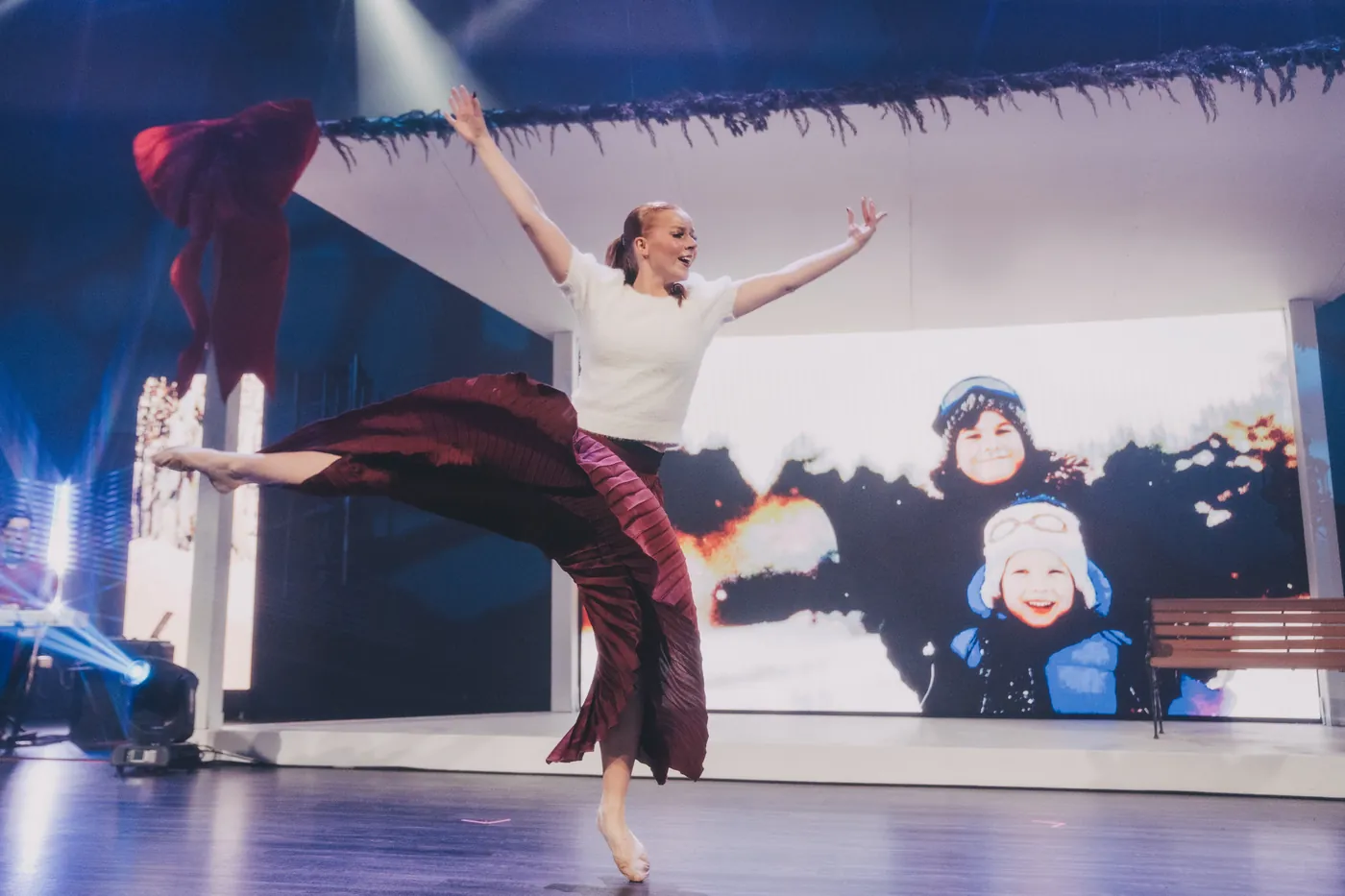 A dancer leaps across the stage, arms wide, in front of a winter scene.