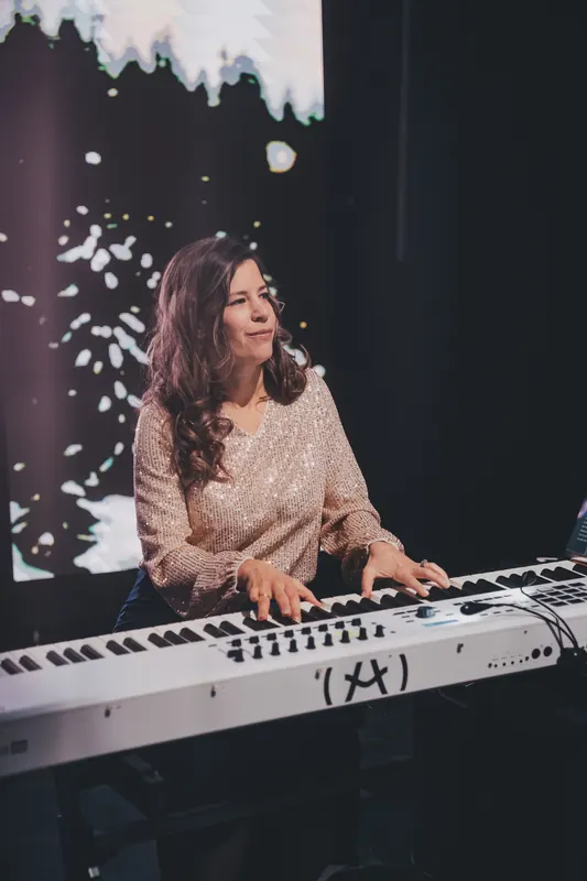 A pianist smiles at the keys as snow drifts down over the stage.