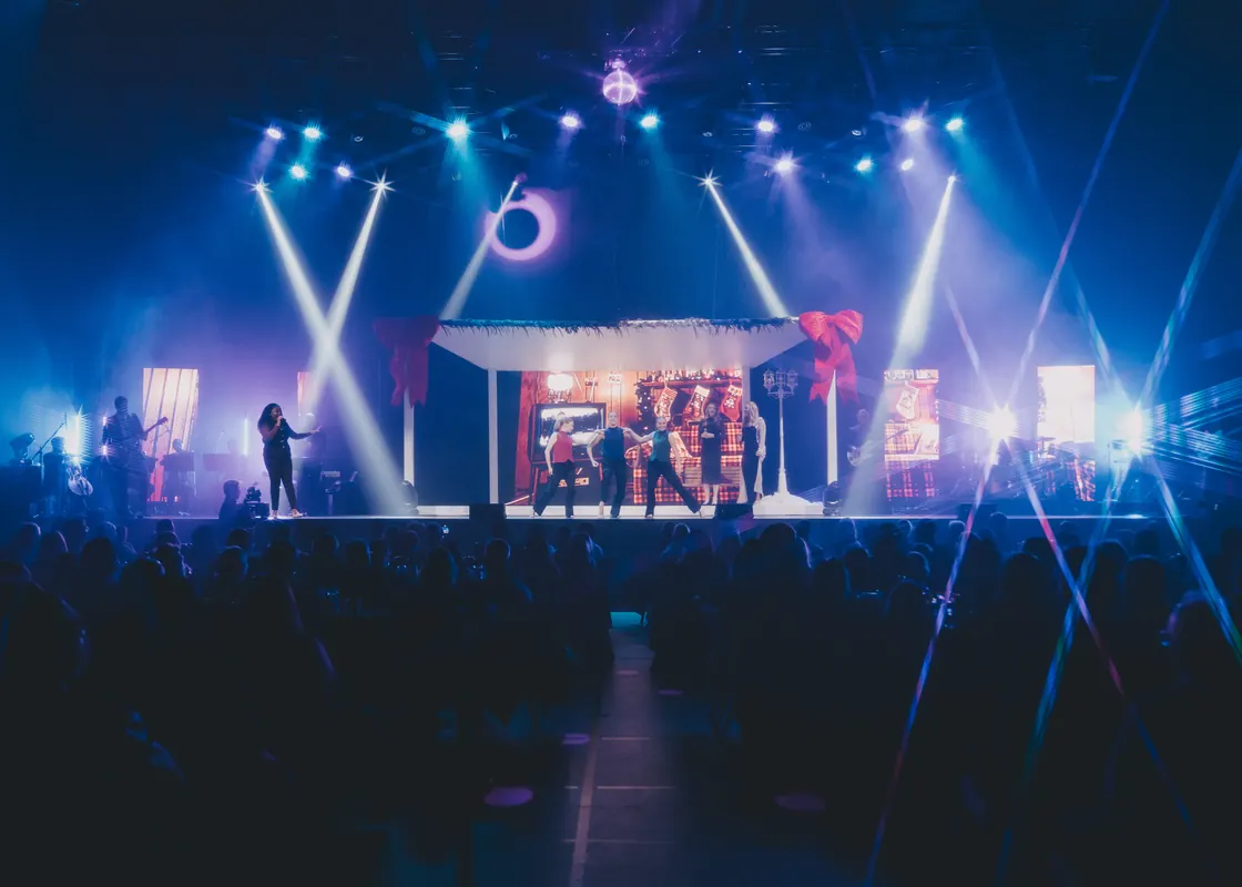 The full A Niagara Christmas stage under blue light beams, the audience in silhouette.