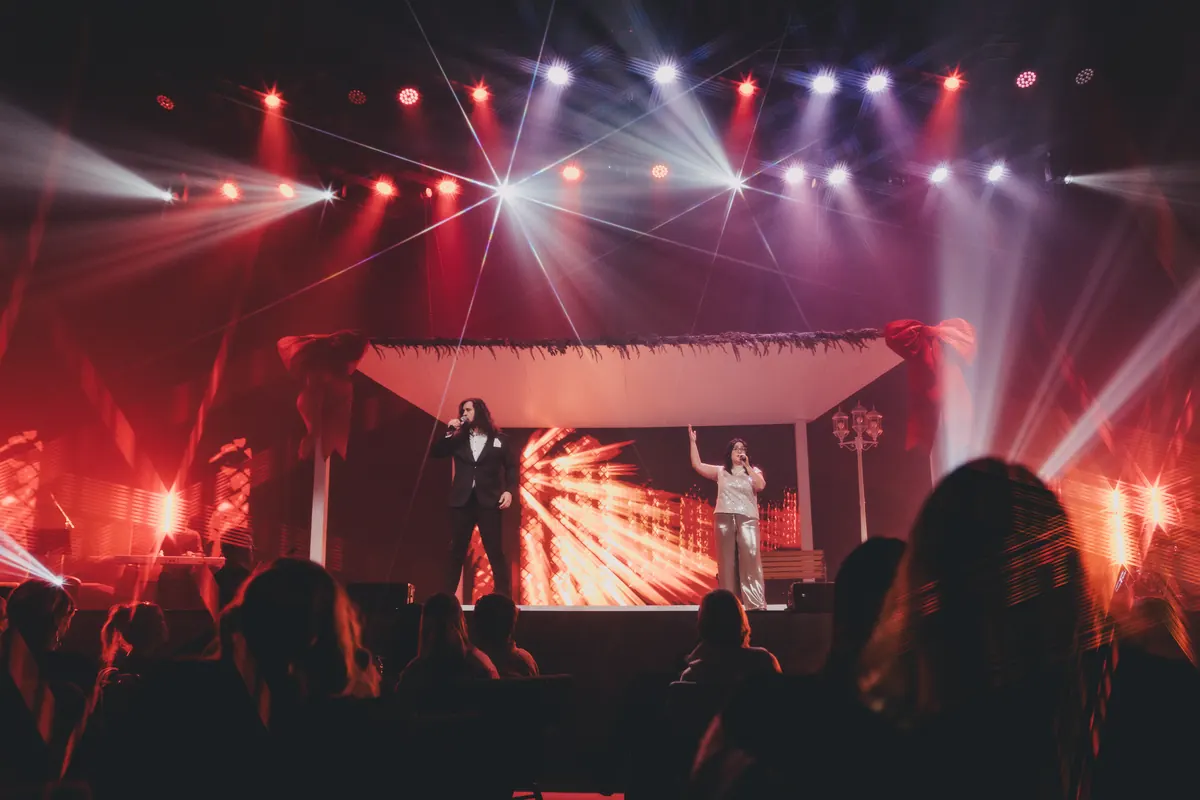 The stage washed in red light, two singers beneath the garland-trimmed canopy.