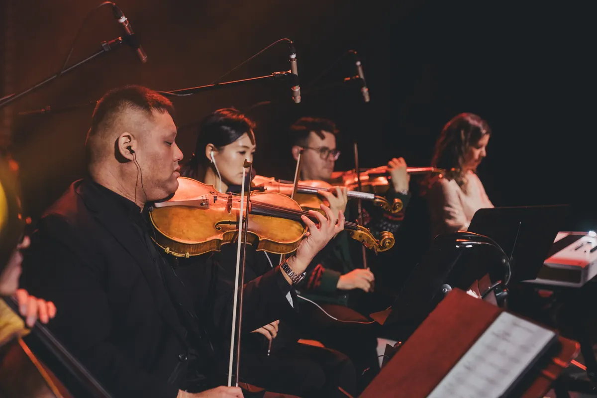 The string section plays, violins raised, in warm stage light.