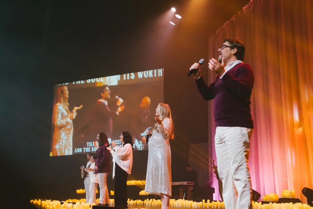 Singers lead a carol on the candlelit Christmas Eve stage, the lyrics on the screen beside them.