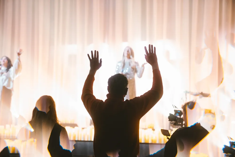 Worshippers raise their hands in silhouette against the bright stage on Christmas Eve.