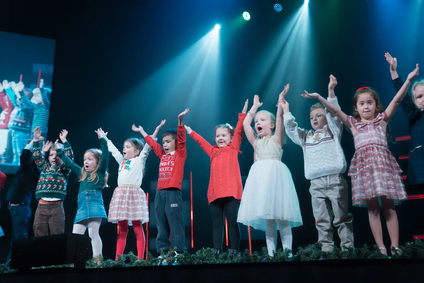 Children on stage throw their arms up under blue stage lights during the Kids Christmas Takeover.
