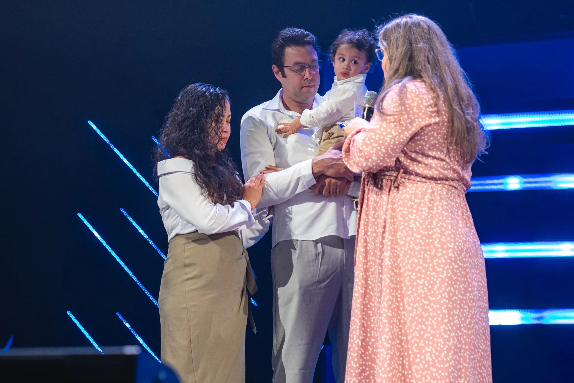 Parents holding their child on stage during a child dedication.