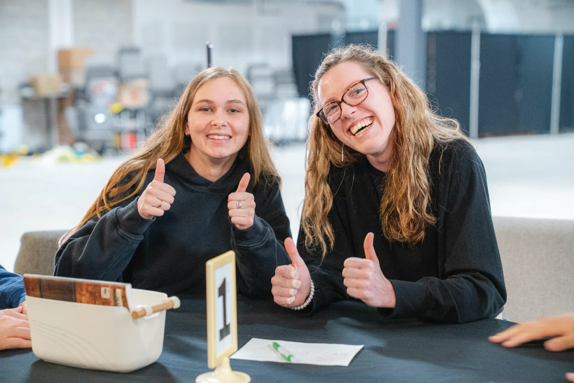 Two young adults at a numbered table giving thumbs up and smiling.