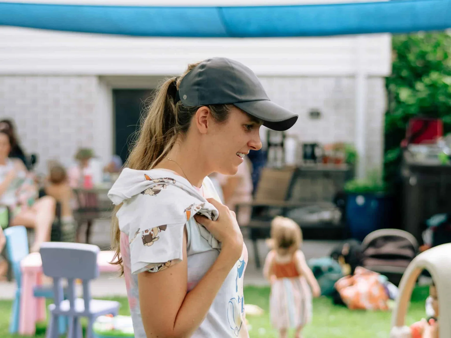 A mom at a backyard meet-up with children playing on the grass behind her.